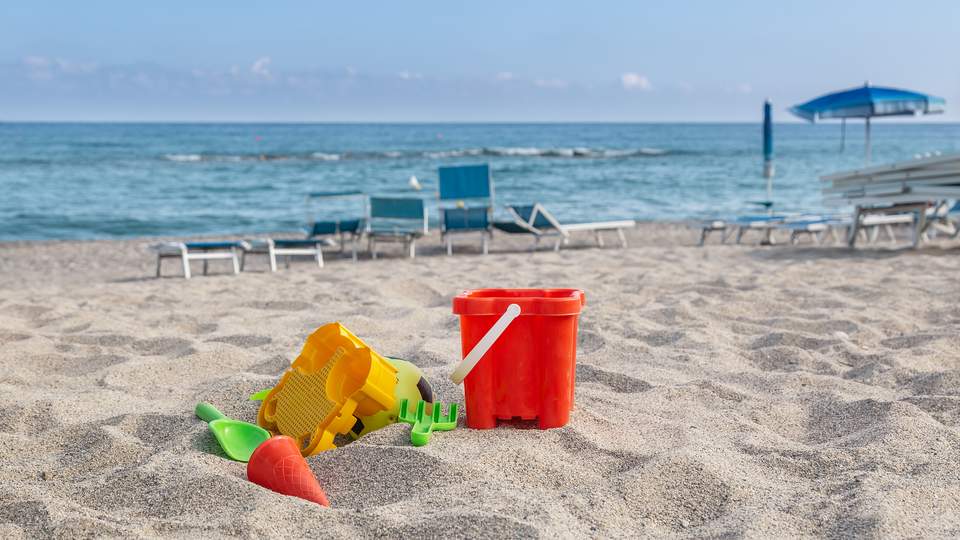 Leeg maar zonnig strand met speelgoed, ligstoelen en een parasol