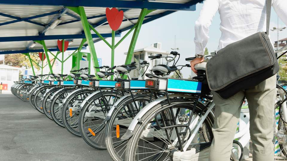 Man met een huurfiets bij een huurfietsenparking.